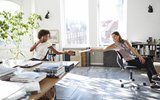 Man riding bike inside an office waving hand to coworkers