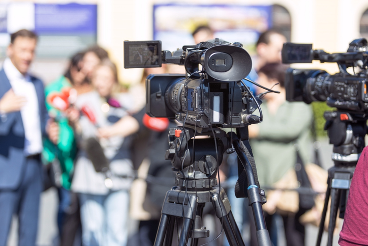 Decorative officials standing in front of news cameras at an event