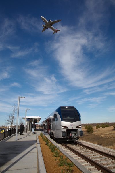 Image of a low-flying plane above a public transportation rail line.