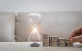 A small hour glass with stacks of coins next to it