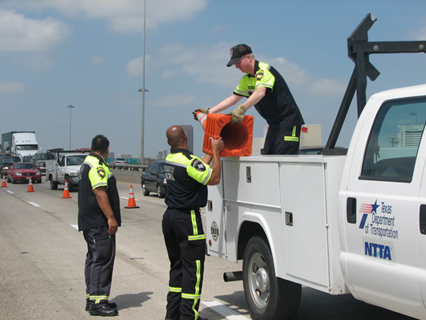 Photo example of traffic incident management with men working to place cones on a road